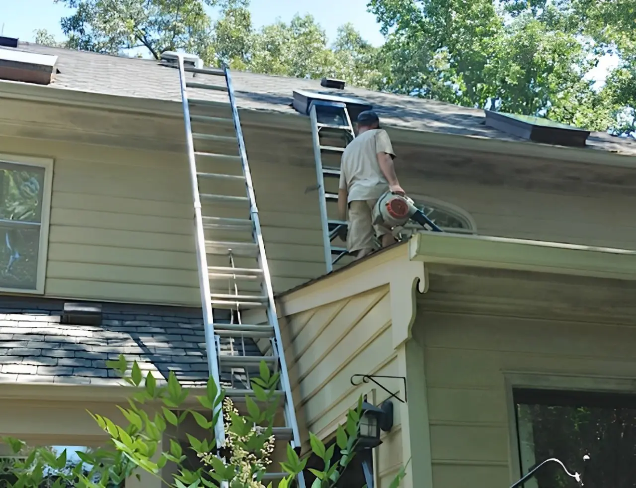 A man on the roof of a house with a ladder.